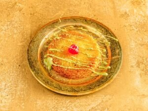 Traditional kunafa dessert topped with pistachio sauce and a red cherry
